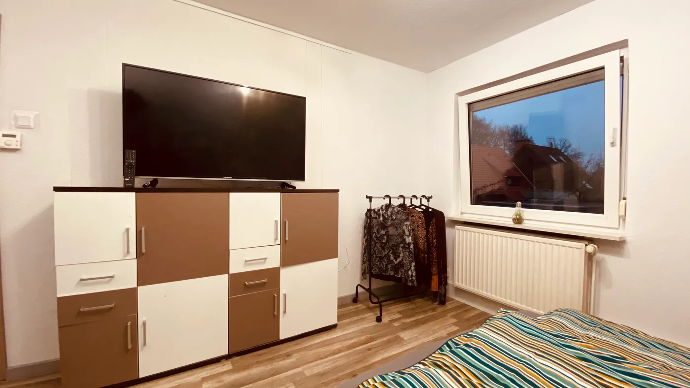 Zweites Zimmer mit Fernseher, Kommode und Kleiderstange